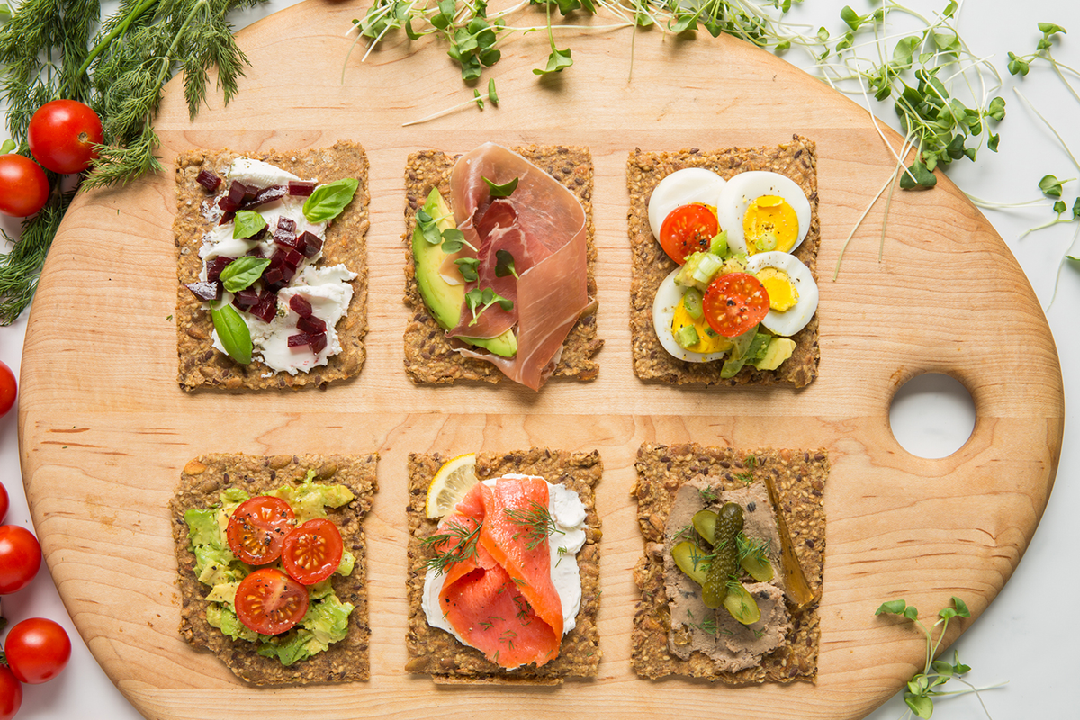 Decorated Wooden cutting board with six crispbread with various spreads and ingredients.
