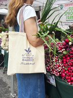 Woman carrying Norwegian Baked tote bag at farmers market with fresh produce vegetables