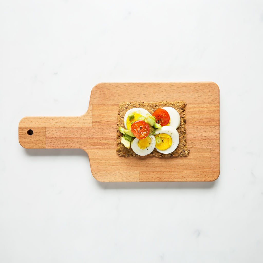 Overhead view of Chili Coriander Knekkebrød on a wooden cutting board with a piece of toast topped with avocado, tomato, and egg.  