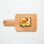 Overhead view of Chili Coriander Knekkebrød on a wooden cutting board with a piece of toast topped with avocado, tomato, and egg.  