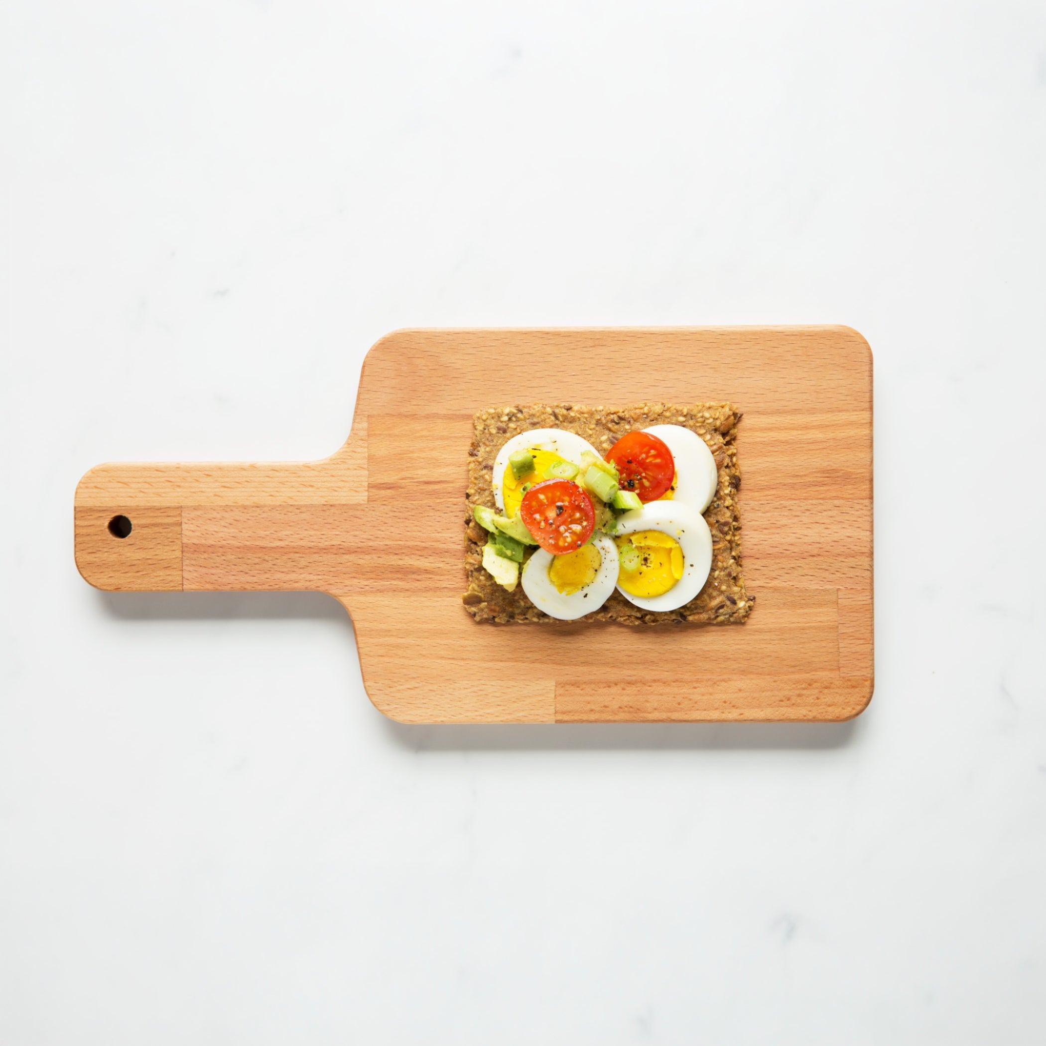 Overhead view of Chili Coriander Knekkebrød on a wooden cutting board with a piece of toast topped with avocado, tomato, and egg.  