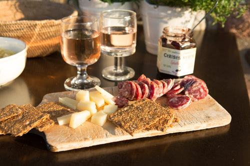 Charcuterie platter of meats, cheeses, and crackers with glasses of wine on a wooden table.