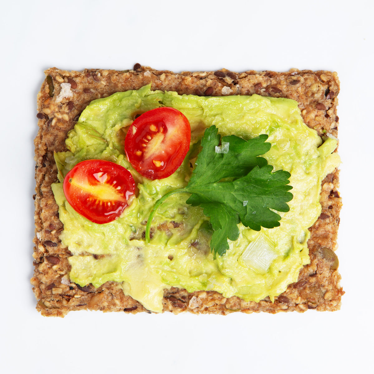 Chili and Coriander Knekkebrød served with avocado spread on a cracker with cherry tomatoes and parsley
