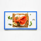 Classic crispbread with smoked salmon, cream cheese, and dill on a white plate with a blue rim. Wholegrain texture.