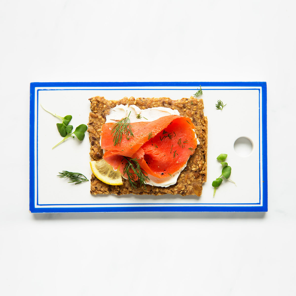 Classic crispbread with smoked salmon, cream cheese, and dill on a white plate with a blue rim. Wholegrain texture.