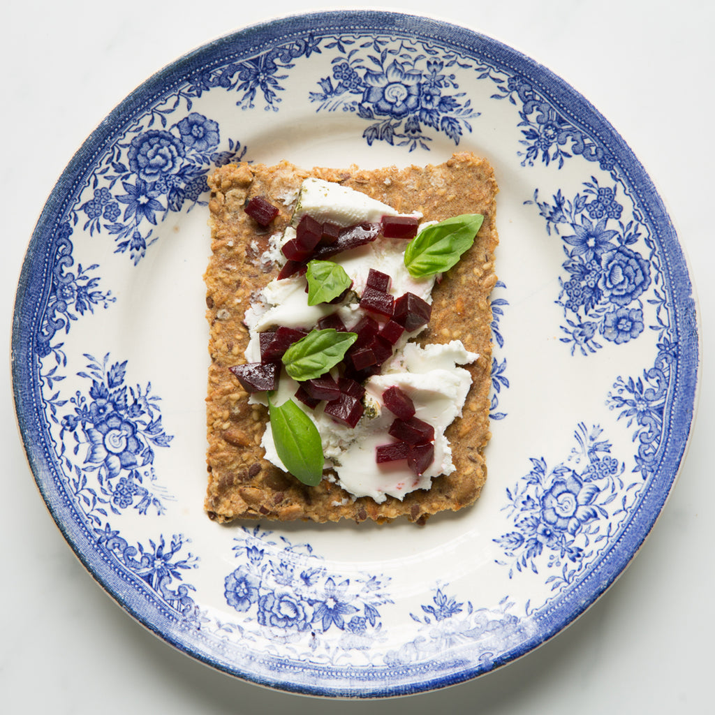 Overhead view of Rosemary Lemon Knekkebrød with cream cheese, beets, and basil on a decorative blue and white plate.