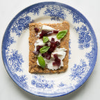 Overhead view of Rosemary Lemon Knekkebrød with cream cheese, beets, and basil on a decorative blue and white plate.