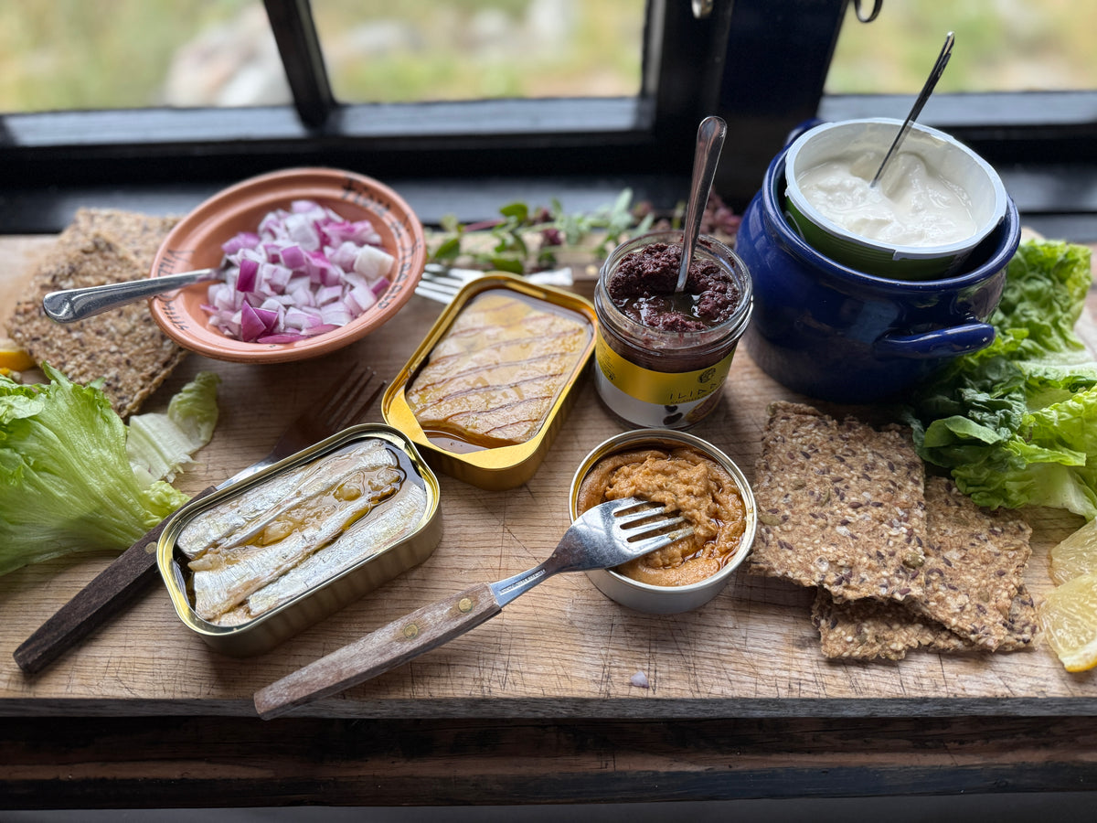 Plated meal with canned fish, pickled vegetables, and Rosemary and Lemon Knekkebrød on a wooden board.